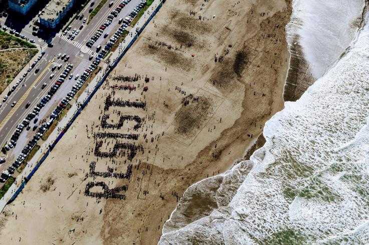 A large number of protesters spell out the words "Resist" on a beach