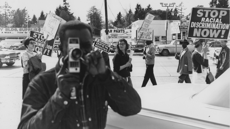 A black and white photo of an activist filming a civil rights protest
