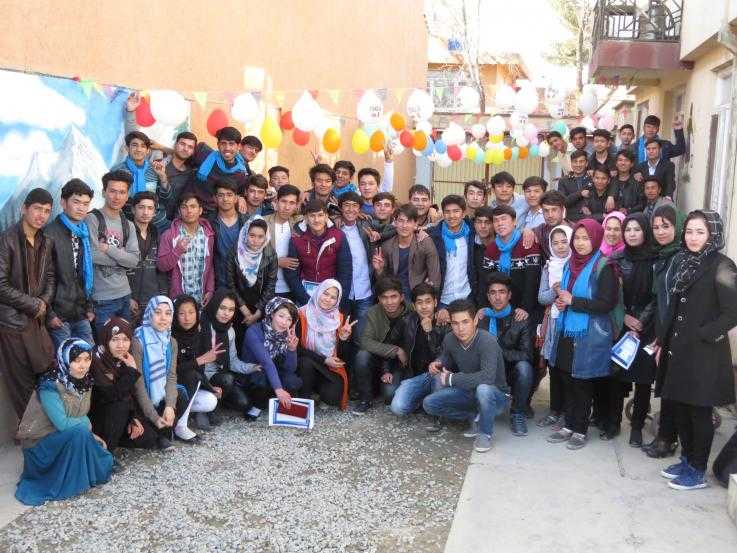 Roughly fifty young people gather for a photo in a street. Some are wearing blue scarves