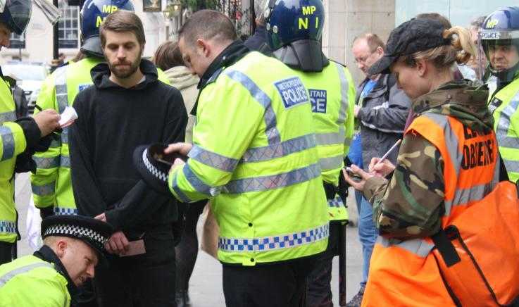 A protester is detained by police as a legal observer looks on and takes notes