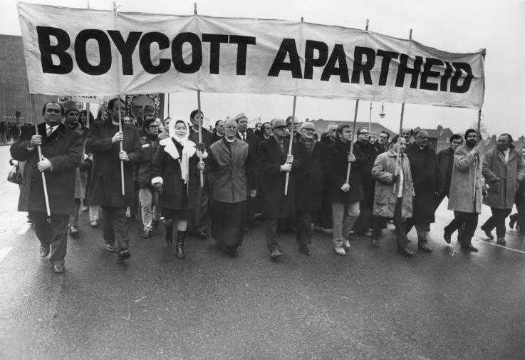 Activist march under a banner reading "Boycott Apartheid"