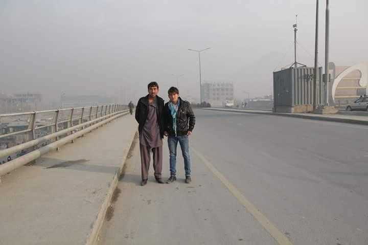 Two men stand in the middle of the photo, in the middle distance. They are on a grey dusty road