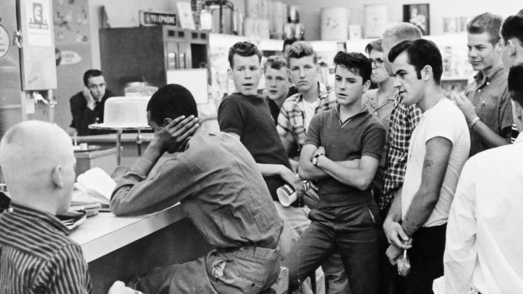 A large group of white young men taunt a black protester during the US civil rights movement.